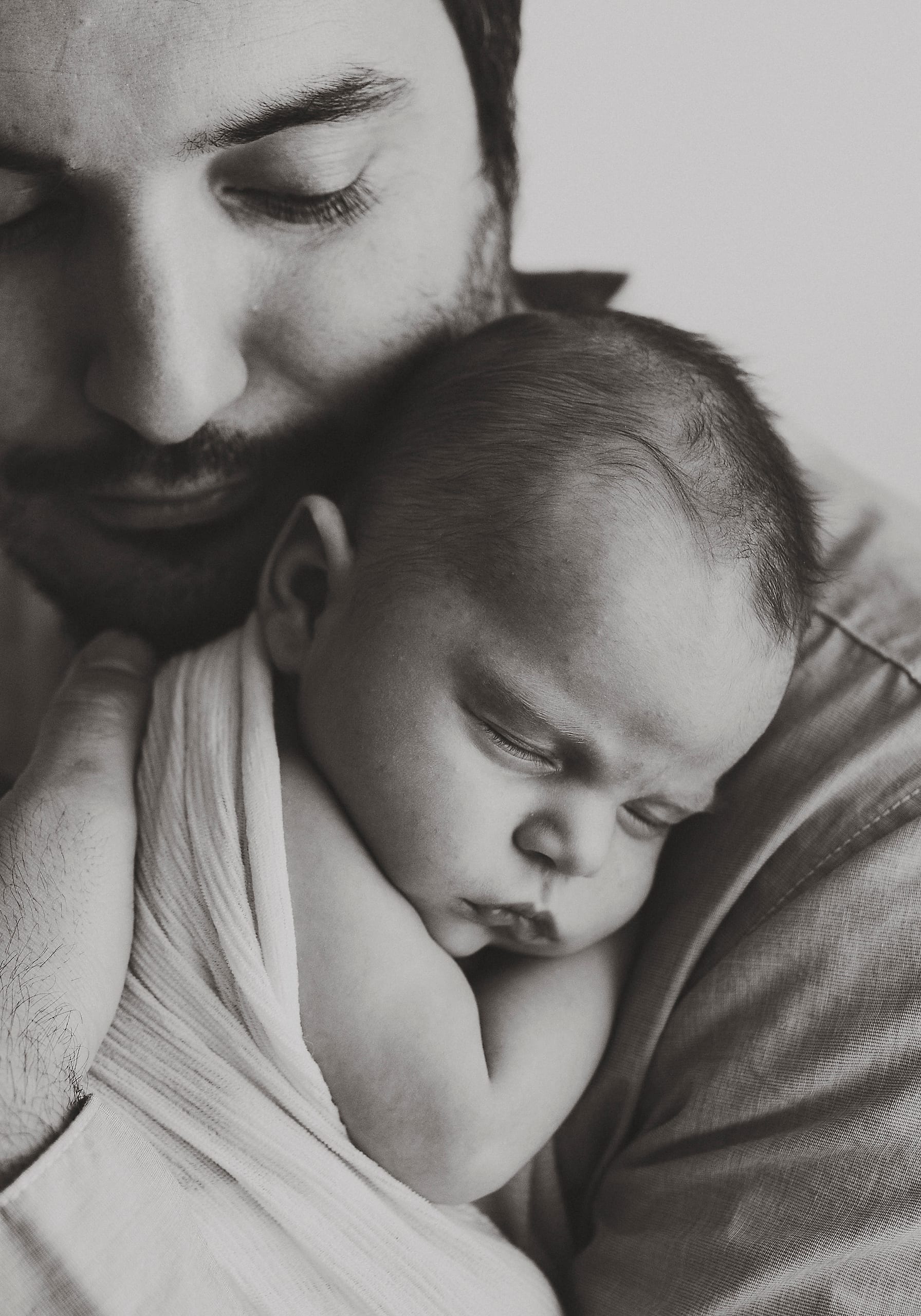 Black and white portrait of a father holding his sleeping newborn against his chest.