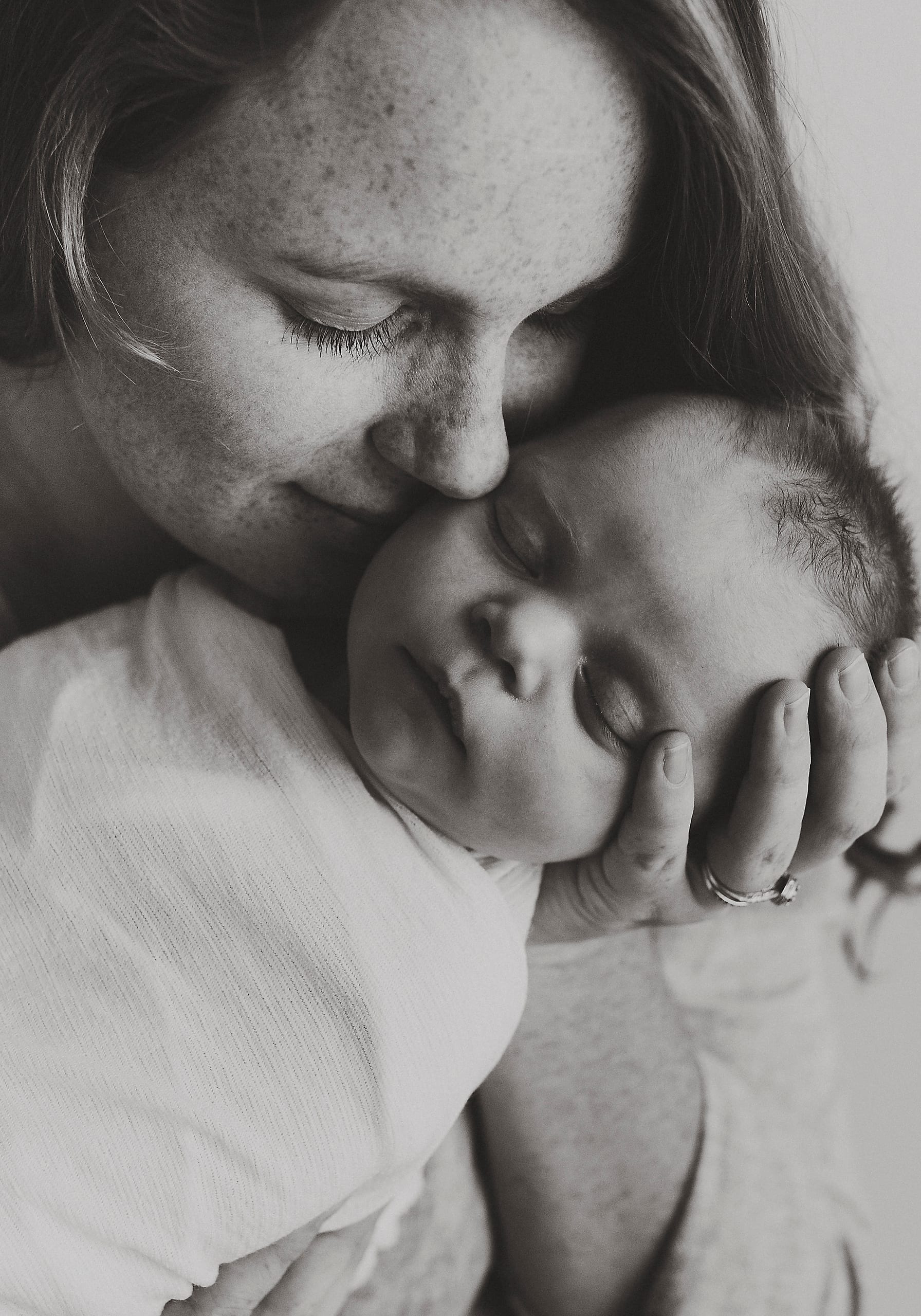 Black and white portrait of a mother nuzzling her sleeping newborn's cheek.