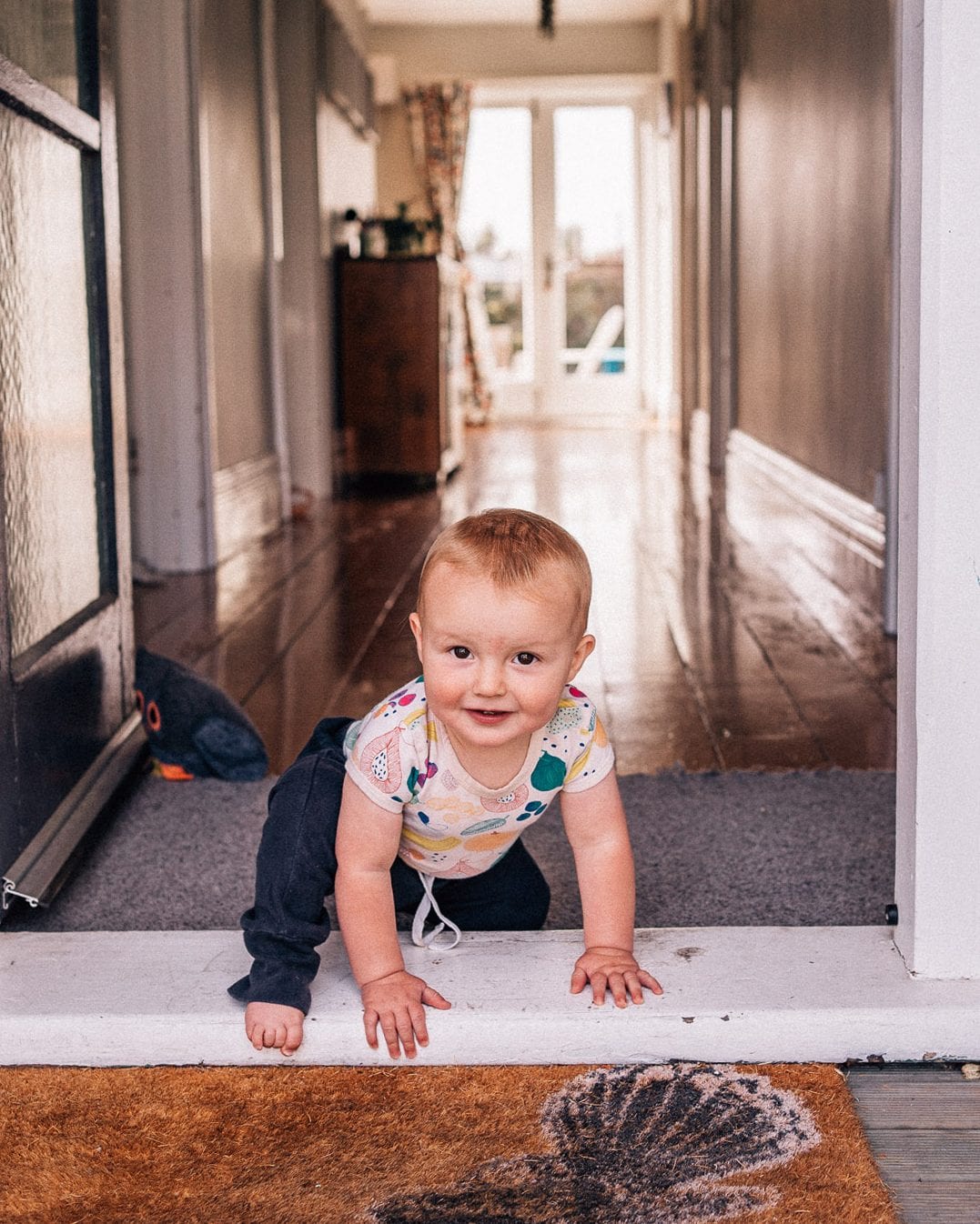 A smiling baby crawls across a sunlit doorway threshold in a character villa hallway.