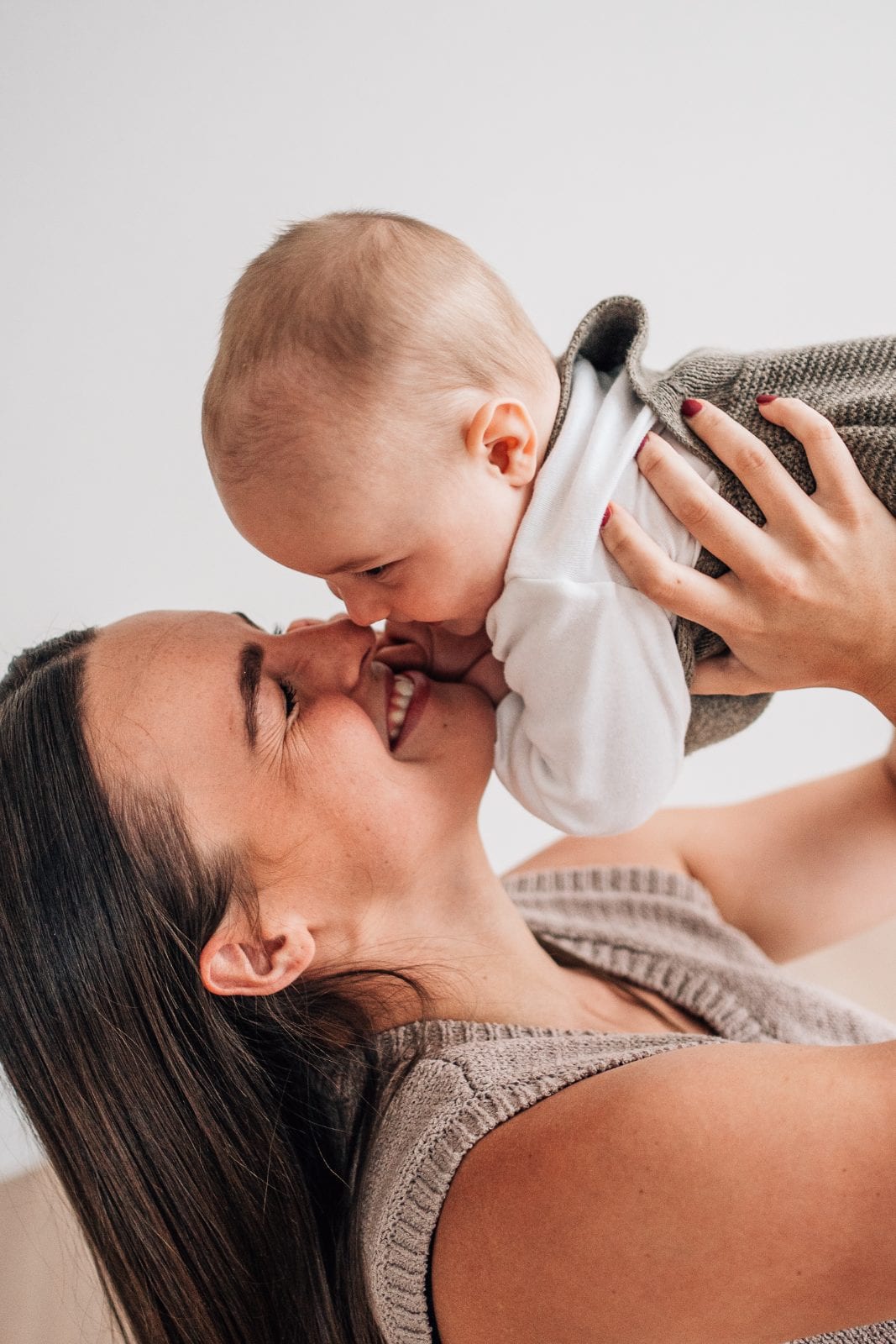 A tiny baby held in a parent’s hands in the window light