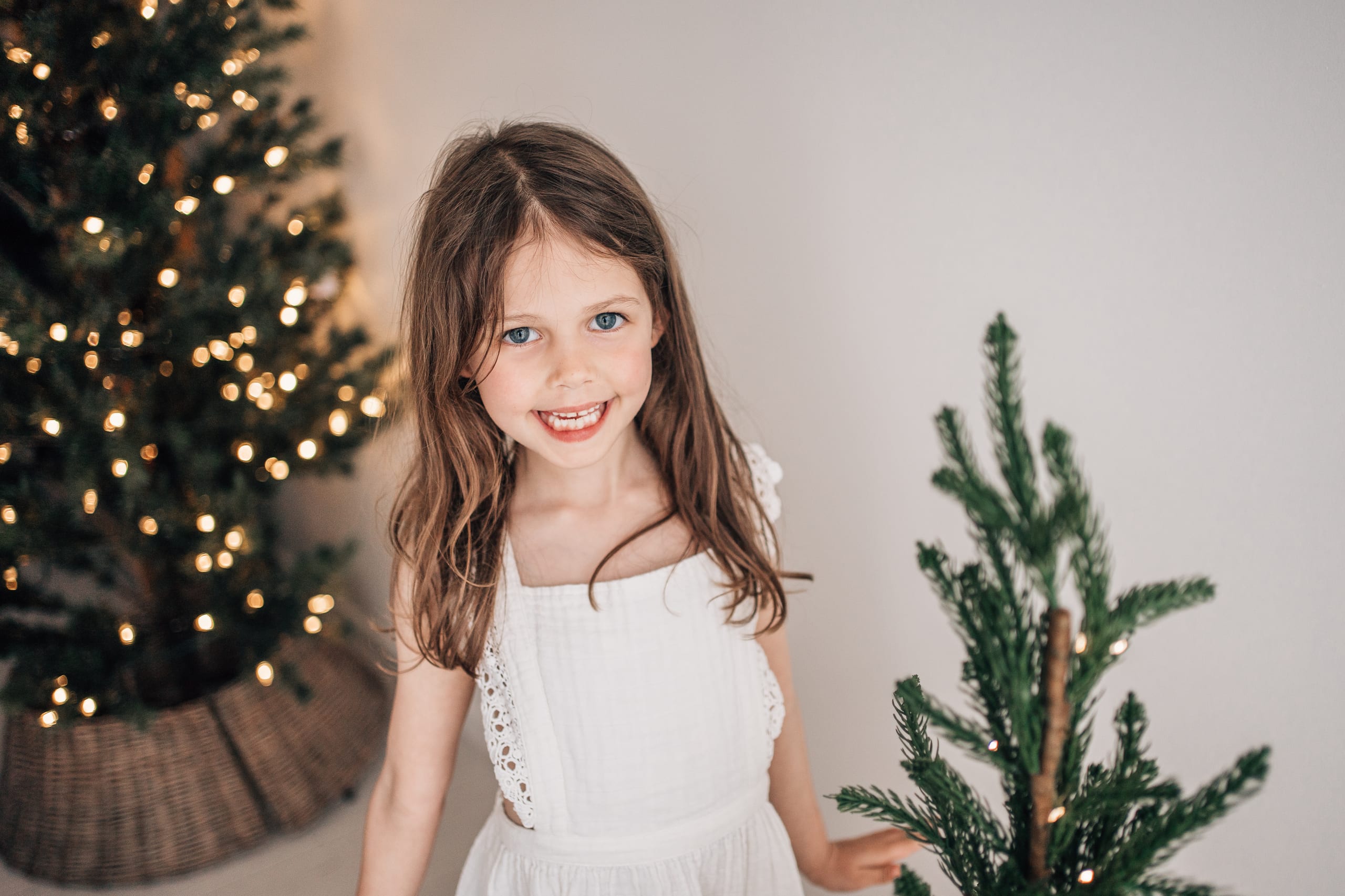 Young girl smiling beside a lit Christmas tree during a festive studio portrait session at The Little White Studio in Lincoln