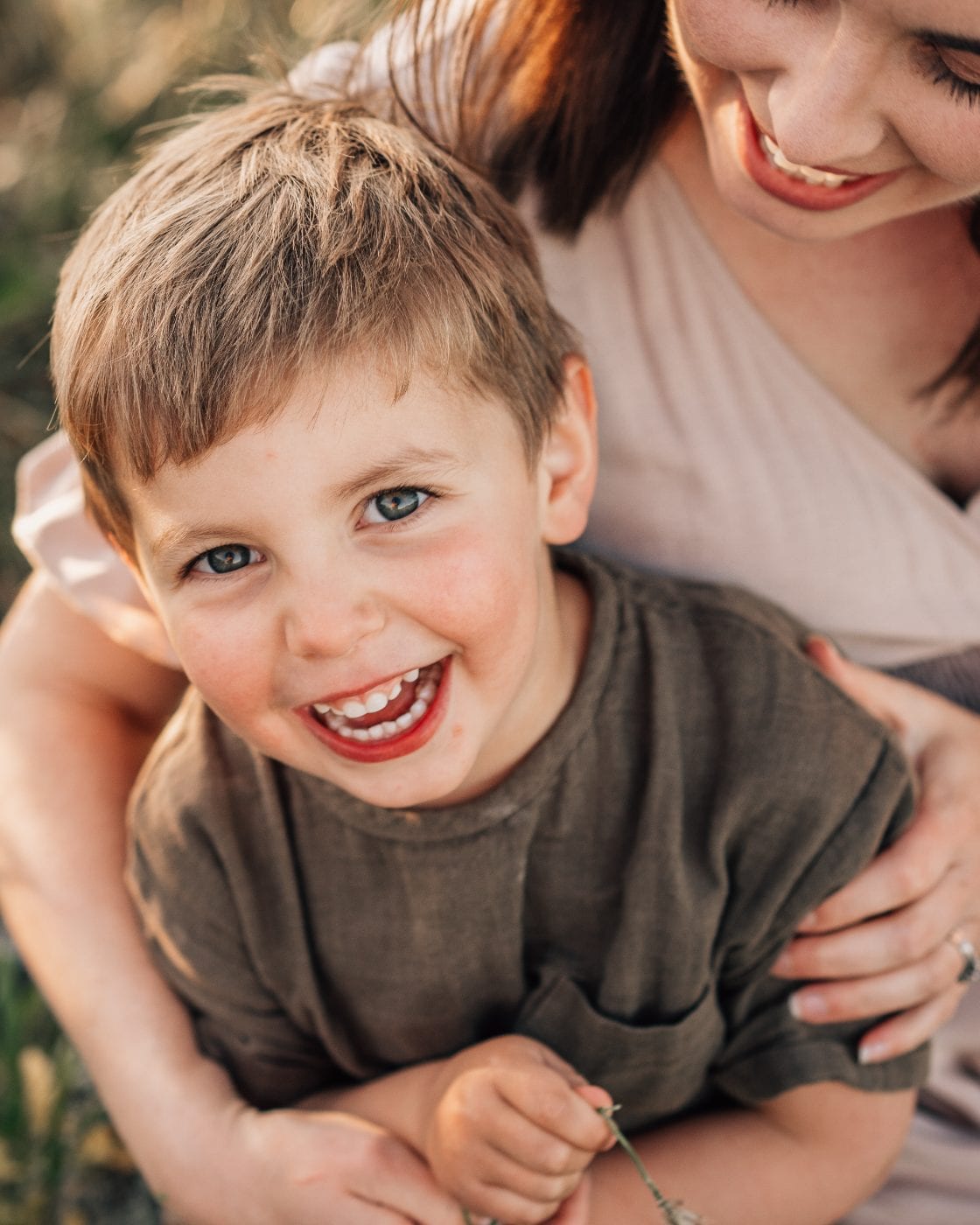A little boy laughing freely in a golden field while his mother holds him close