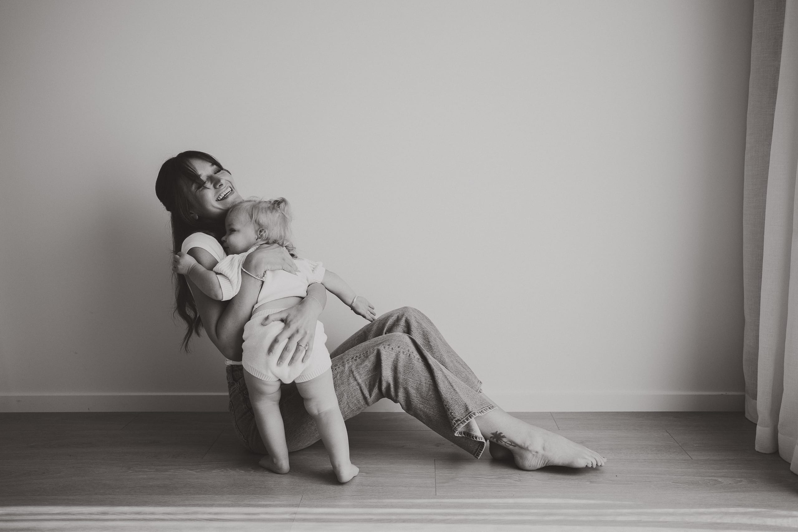 A mother laughing as she cuddles her toddler close on the studio floor.