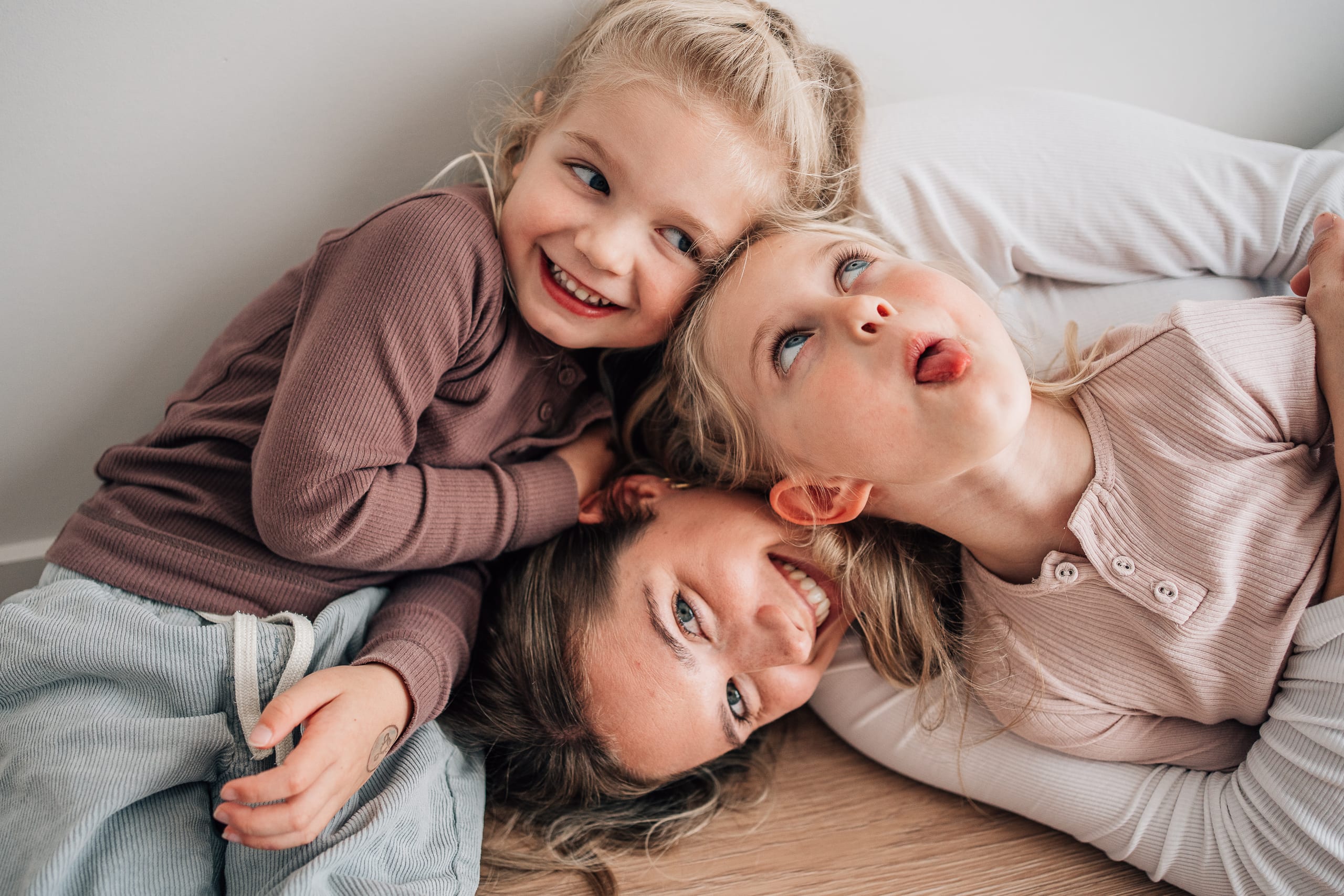 A mother and her two daughters pulling silly faces and poking out tongues together on the studio floor.