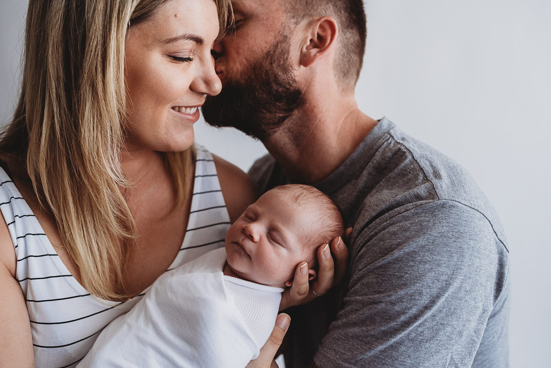 New parents holding their swaddled newborn close during a session at The Little White Studio