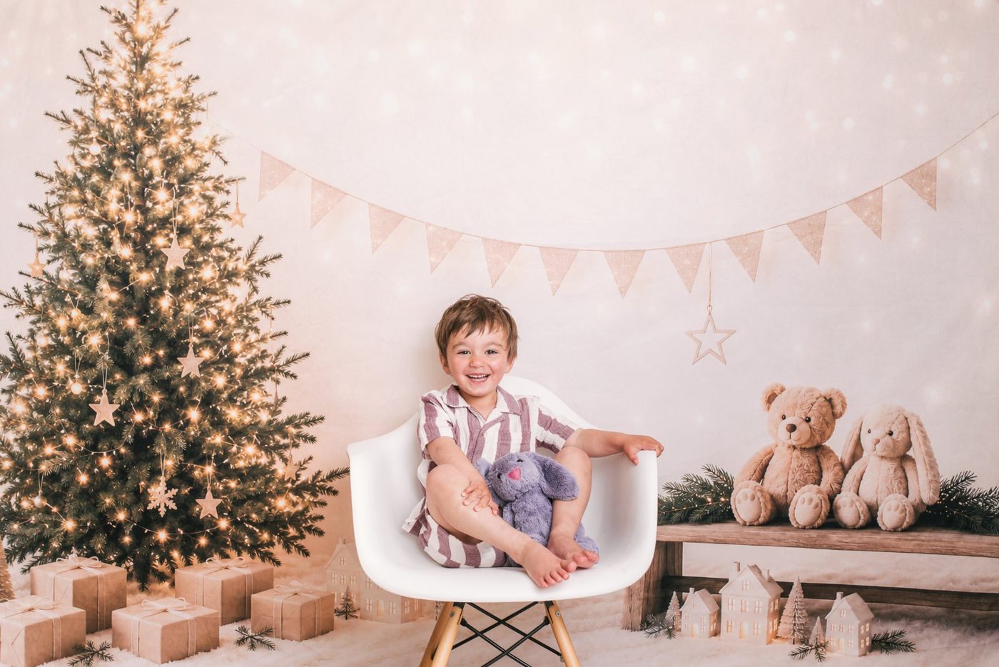 A little boy laughing on the white chair beside this year's Christmas tree at Little Portrait Club