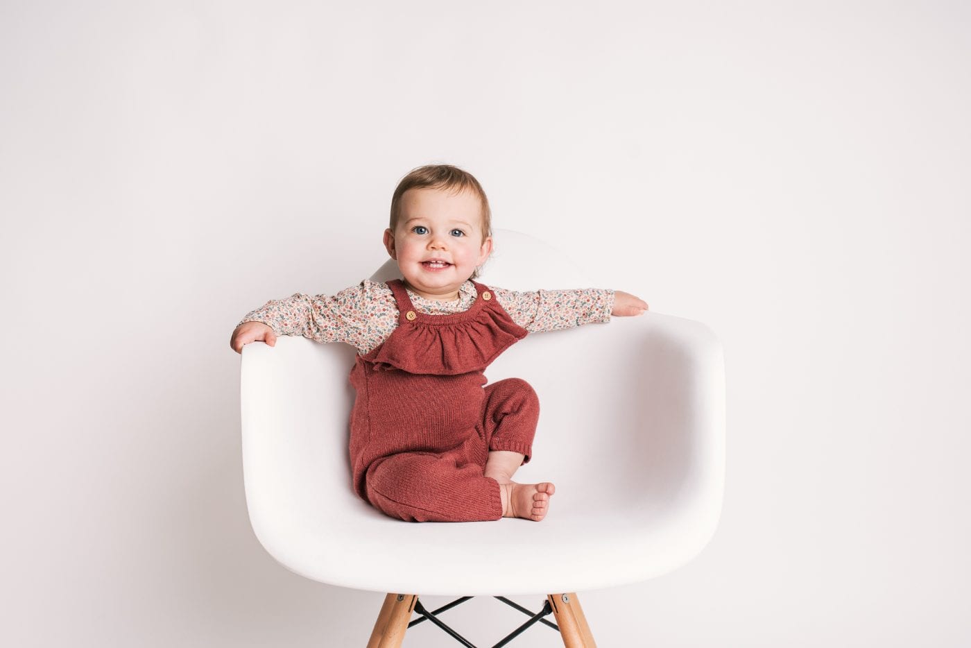 A toddler in rust dungarees standing tall with arms outstretched