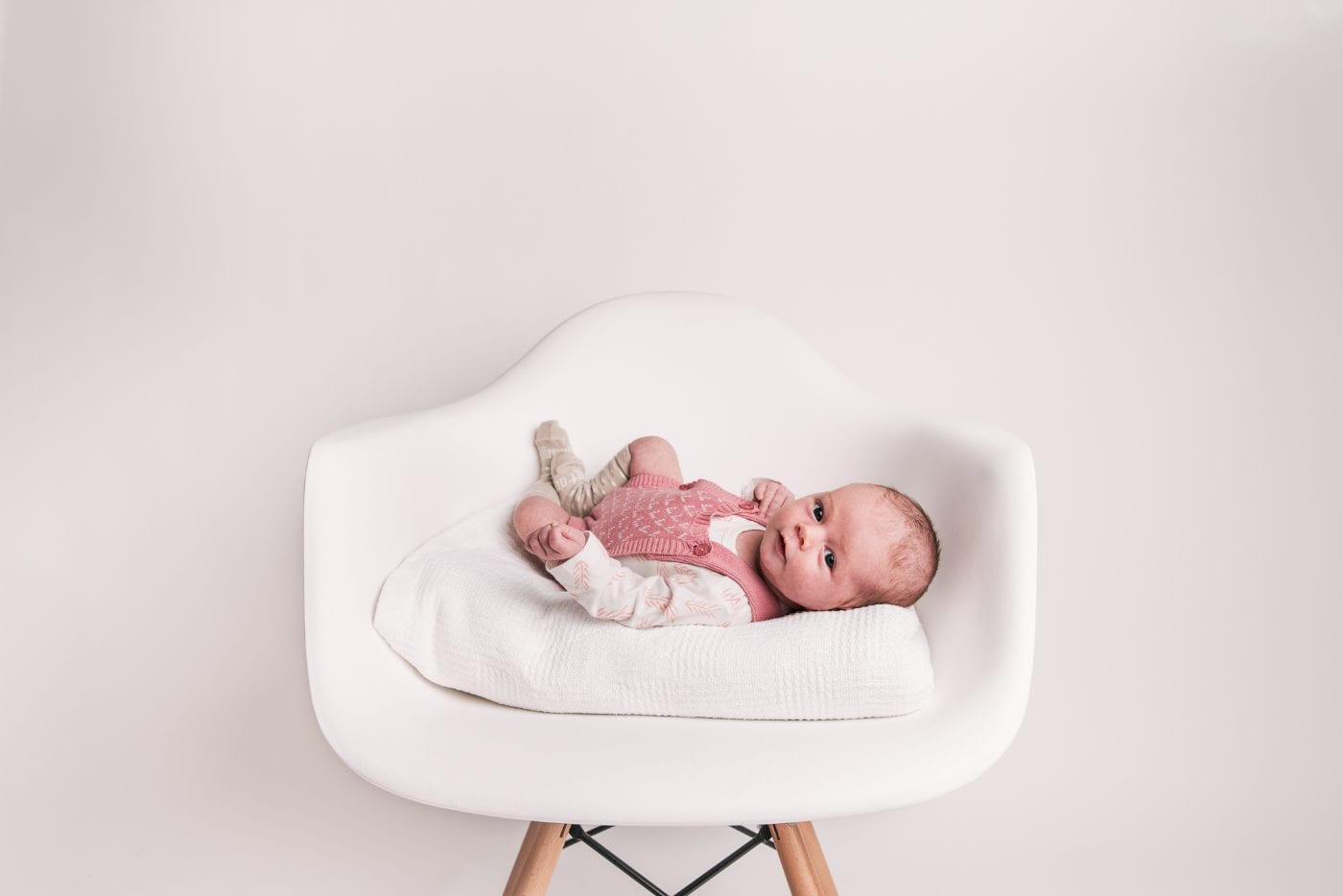 A newborn baby in a knitted pink outfit reclined on a cushion in the studio