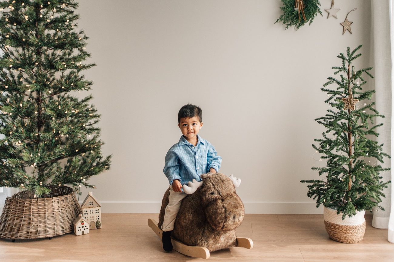 Toddler riding a plush rocking moose in front of the Christmas trees