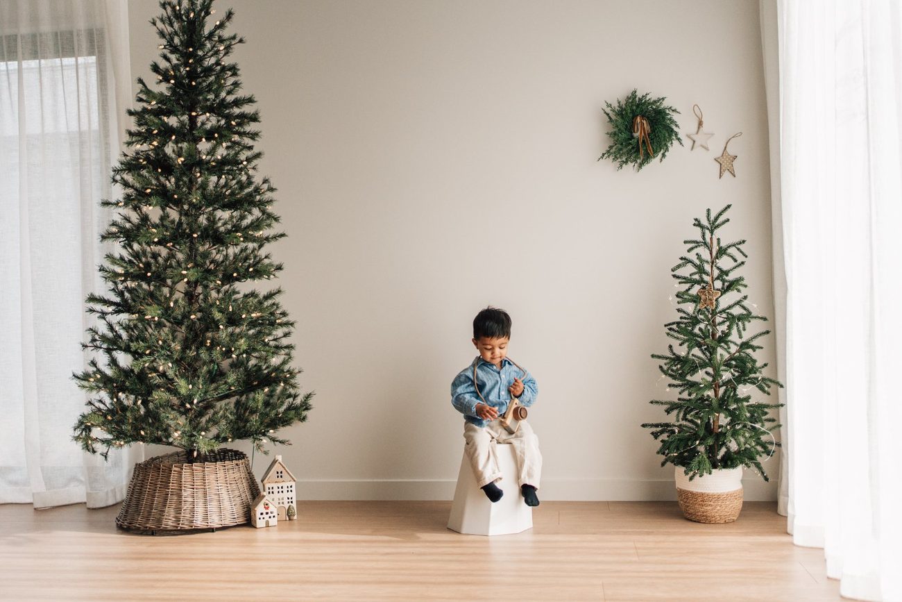 Toddler looking down at his toy camera in the Christmas studio set, sheer curtains either side