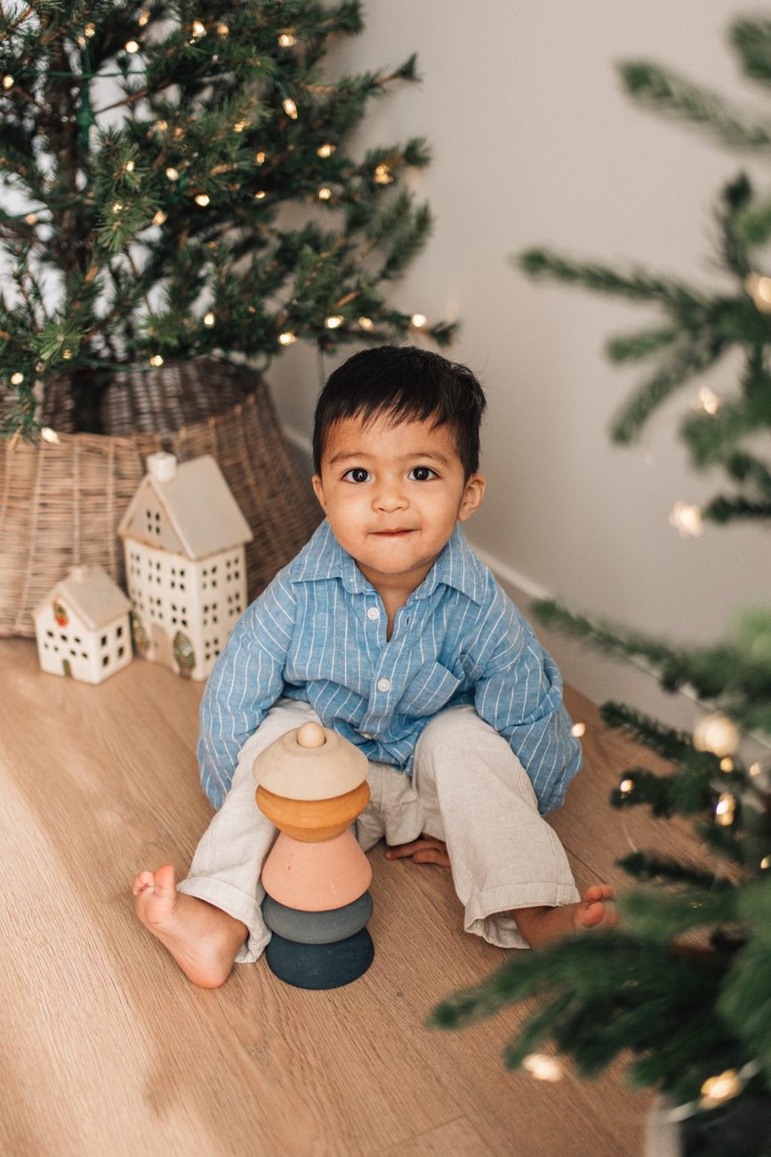 Toddler sitting on the floor by the Christmas tree with a wooden stacking toy