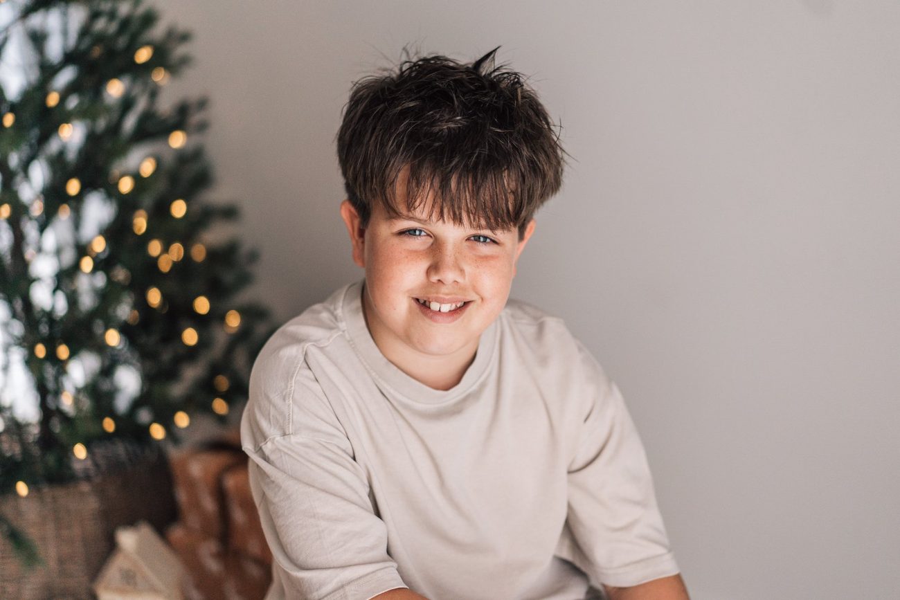 Older brother grinning in front of a softly lit Christmas tree