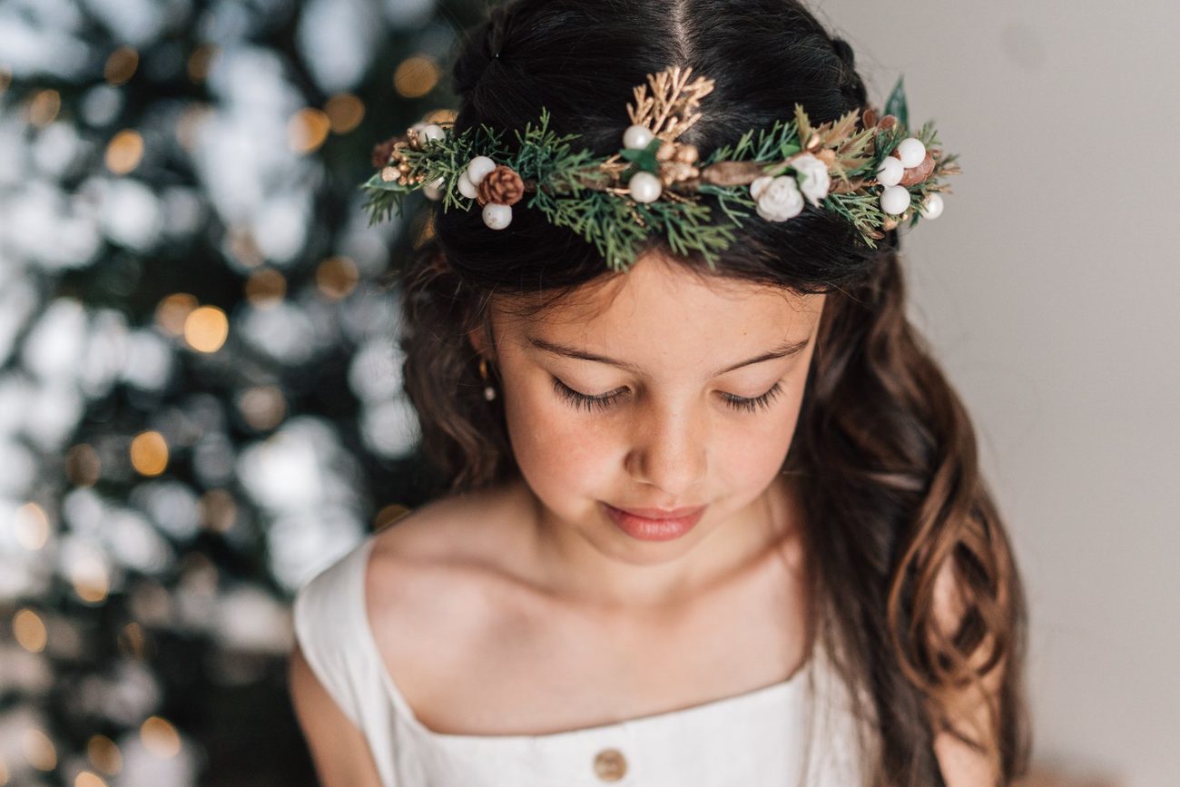 Girl in a festive crown looking down, Christmas lights behind