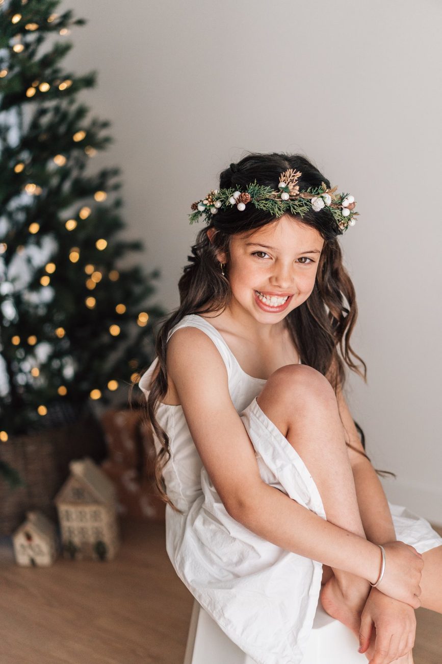 Girl in a festive crown laughing, Christmas tree lights glowing softly behind her