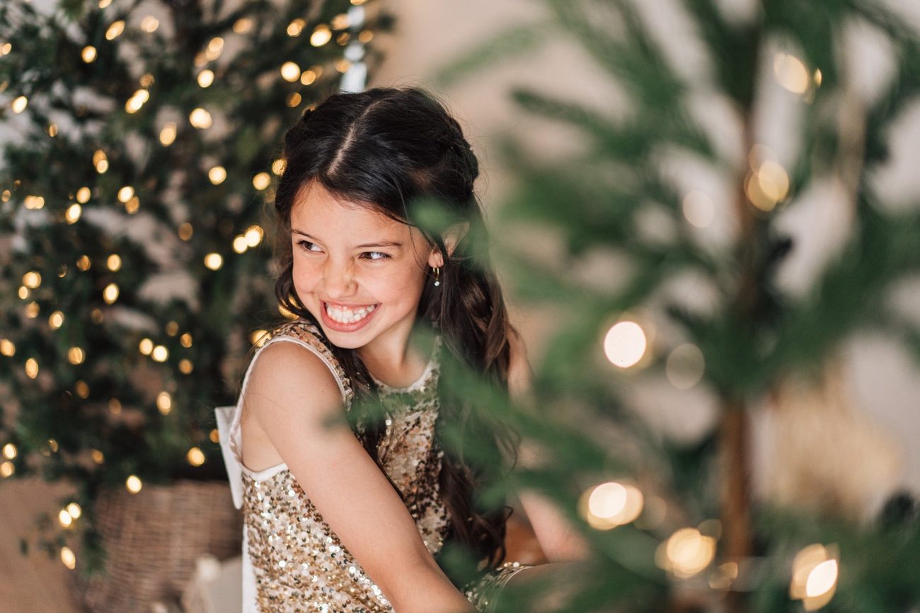 Girl in a sequin dress glancing back through the Christmas tree branches