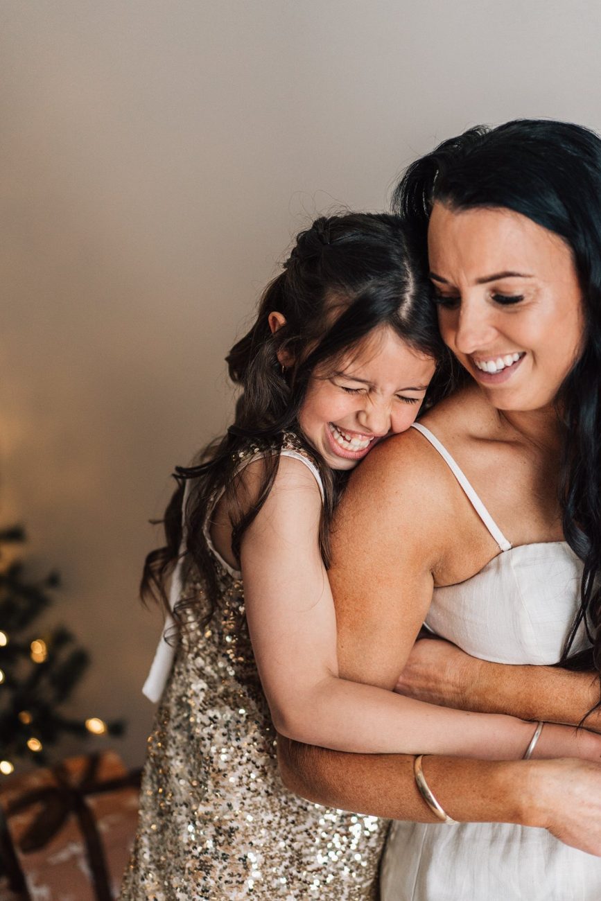 Daughter laughing as she hugs her mum from behind