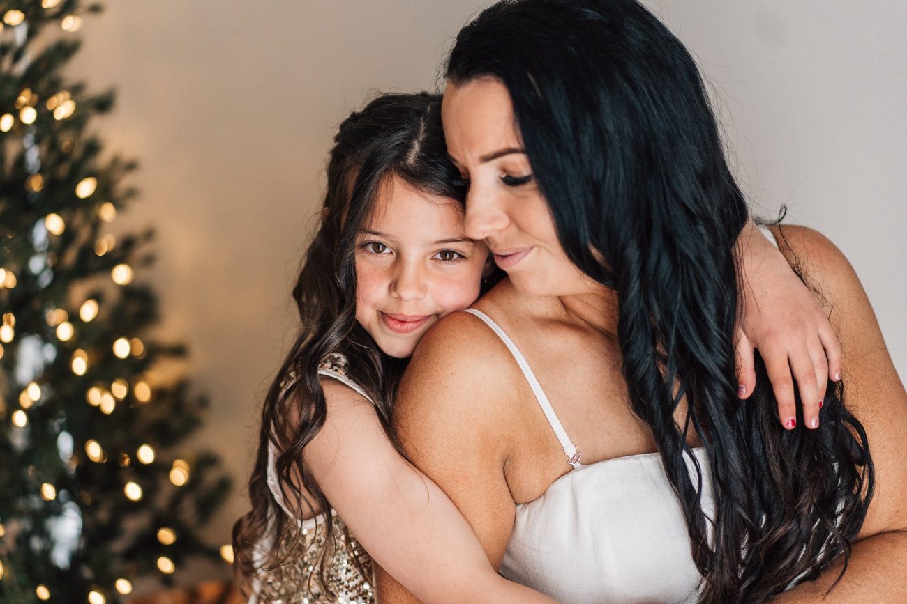 Mum and daughter cuddled cheek to cheek by the Christmas tree