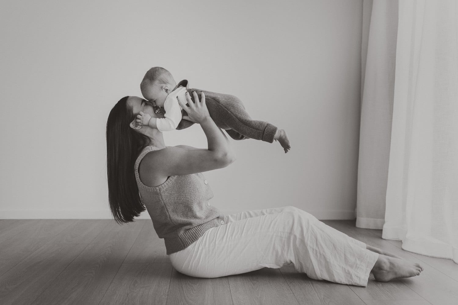 A mother lifting her baby up in a black and white studio portrait