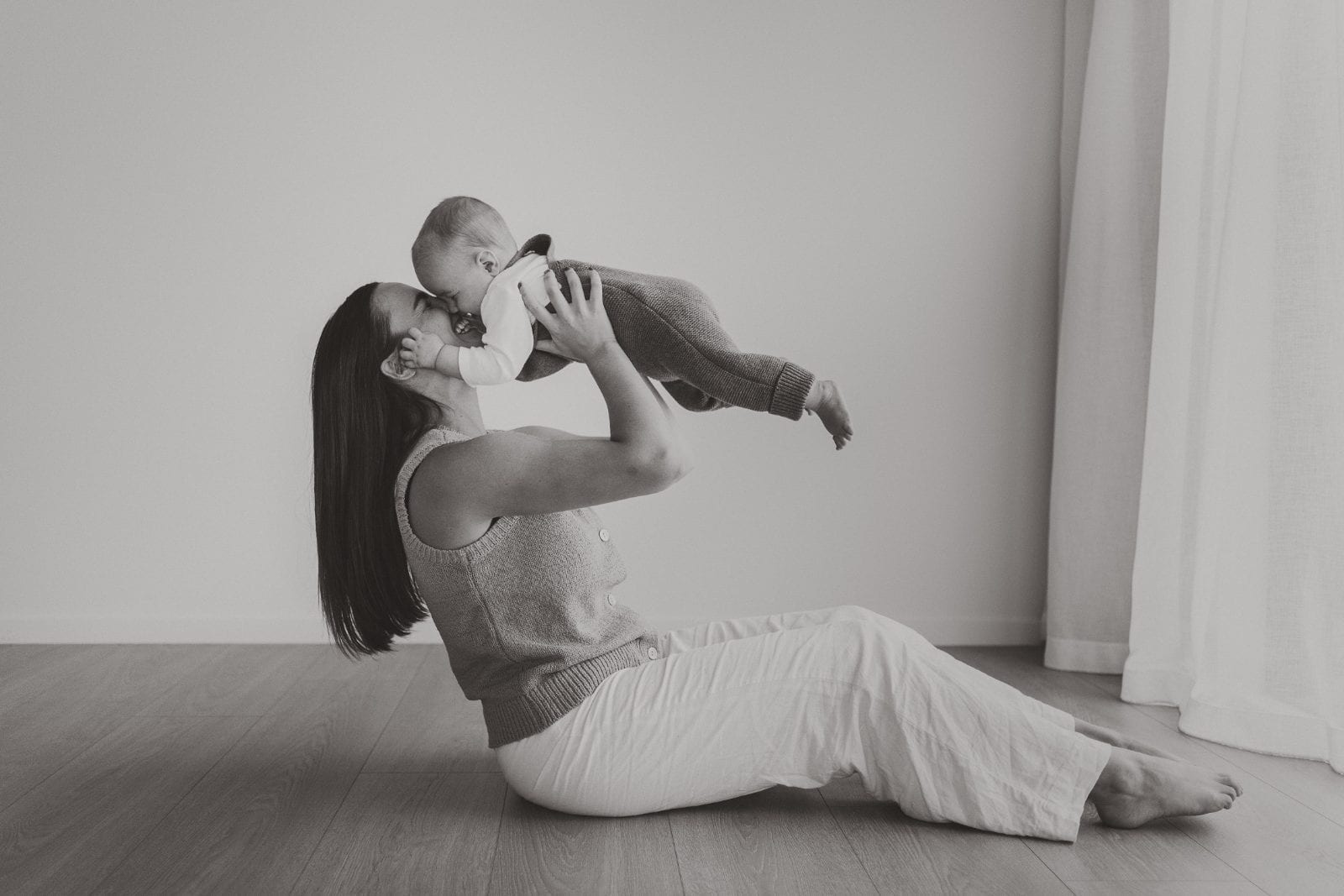 A mother lifting her baby up in a black and white studio portrait