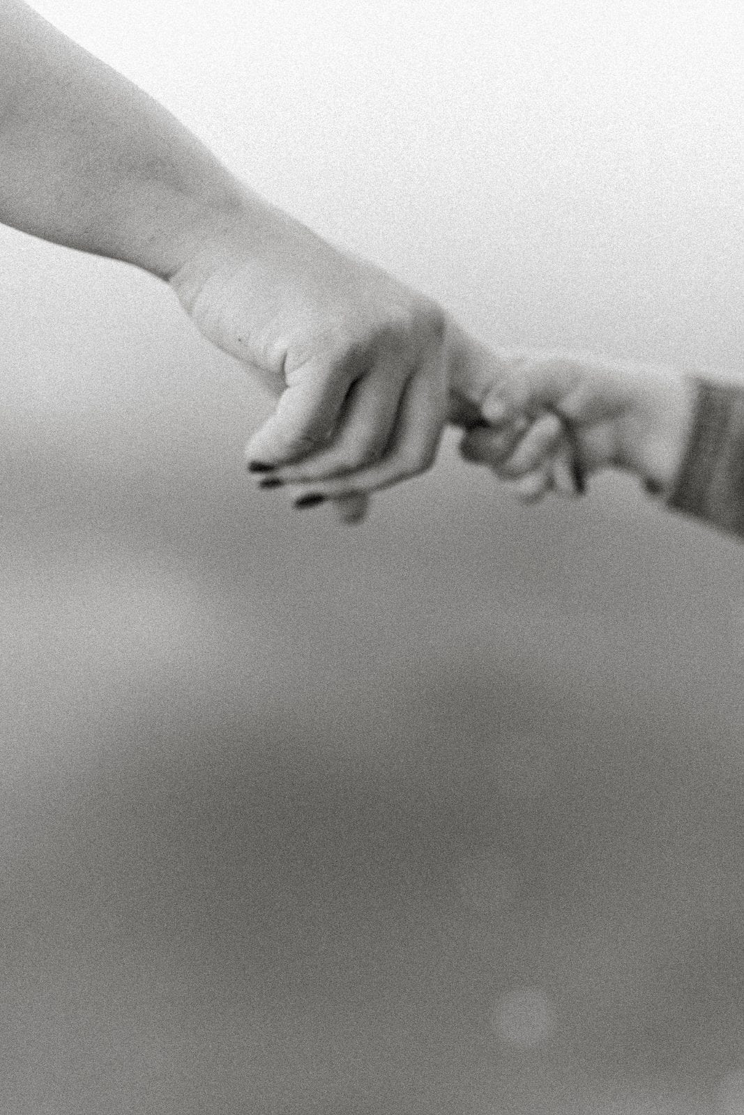 Black and white close-up of a parent and child holding hands, a tender family connection.