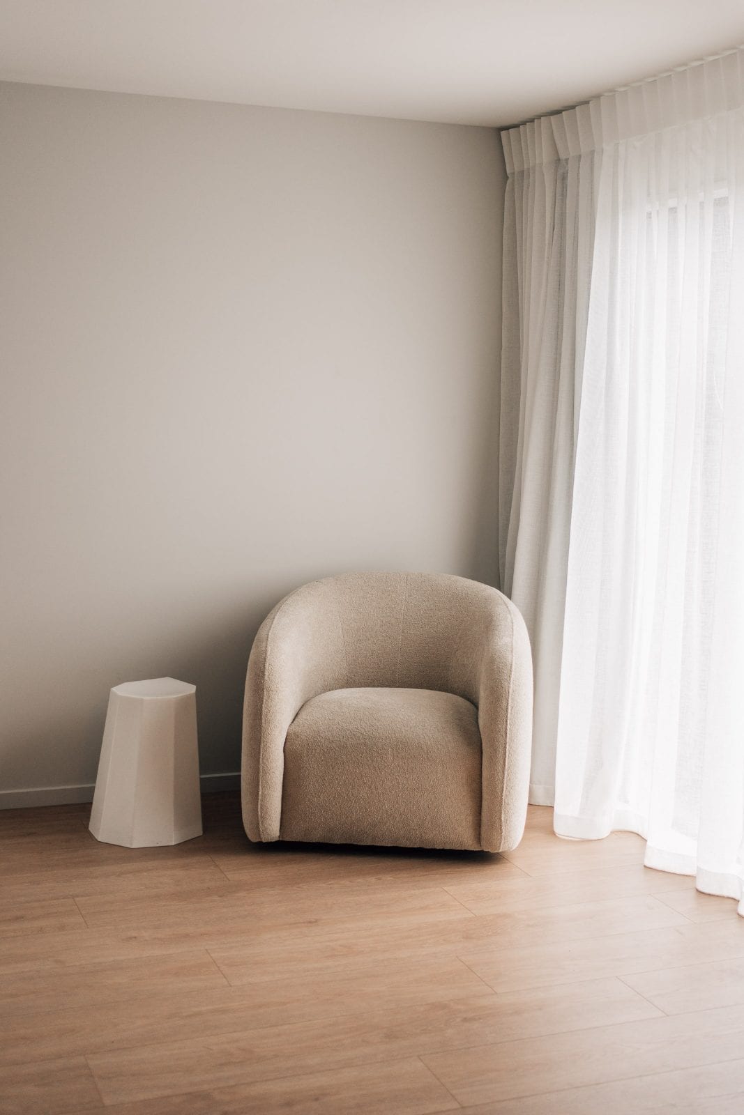 Curved boucle armchair and sculptural side table by sheer curtains in a quiet corner of our Lincoln, Canterbury portrait studio.