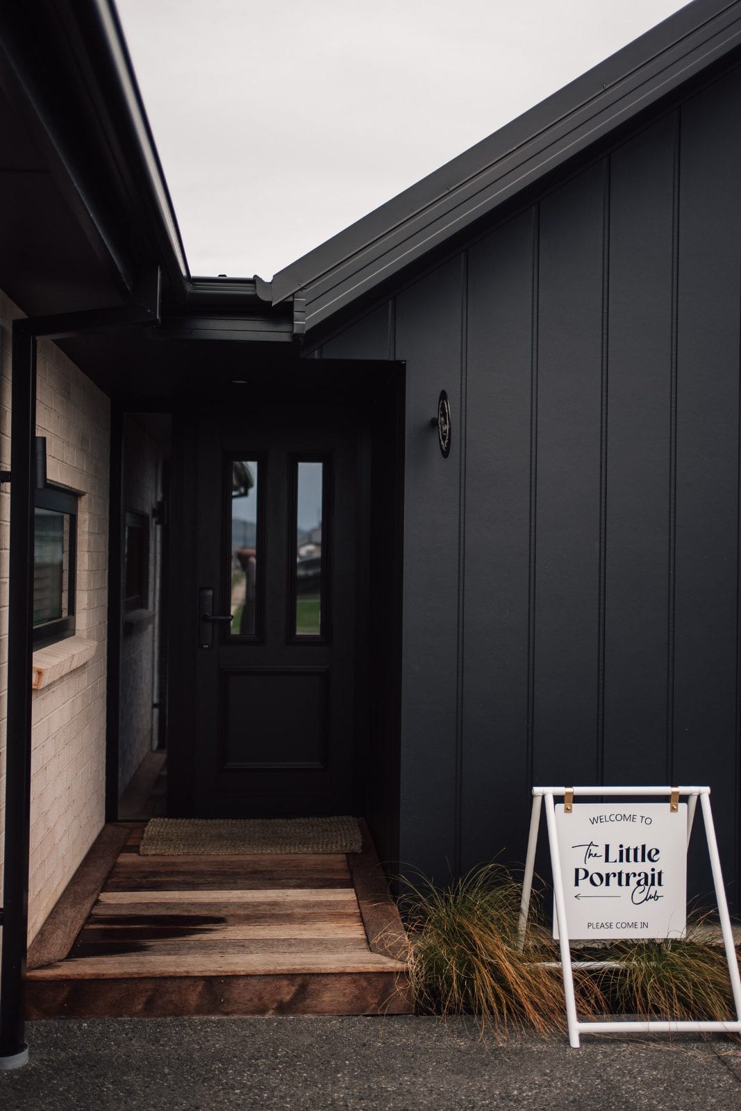 Black weatherboard exterior and front door with the welcome sign at our Lincoln, Canterbury portrait studio.