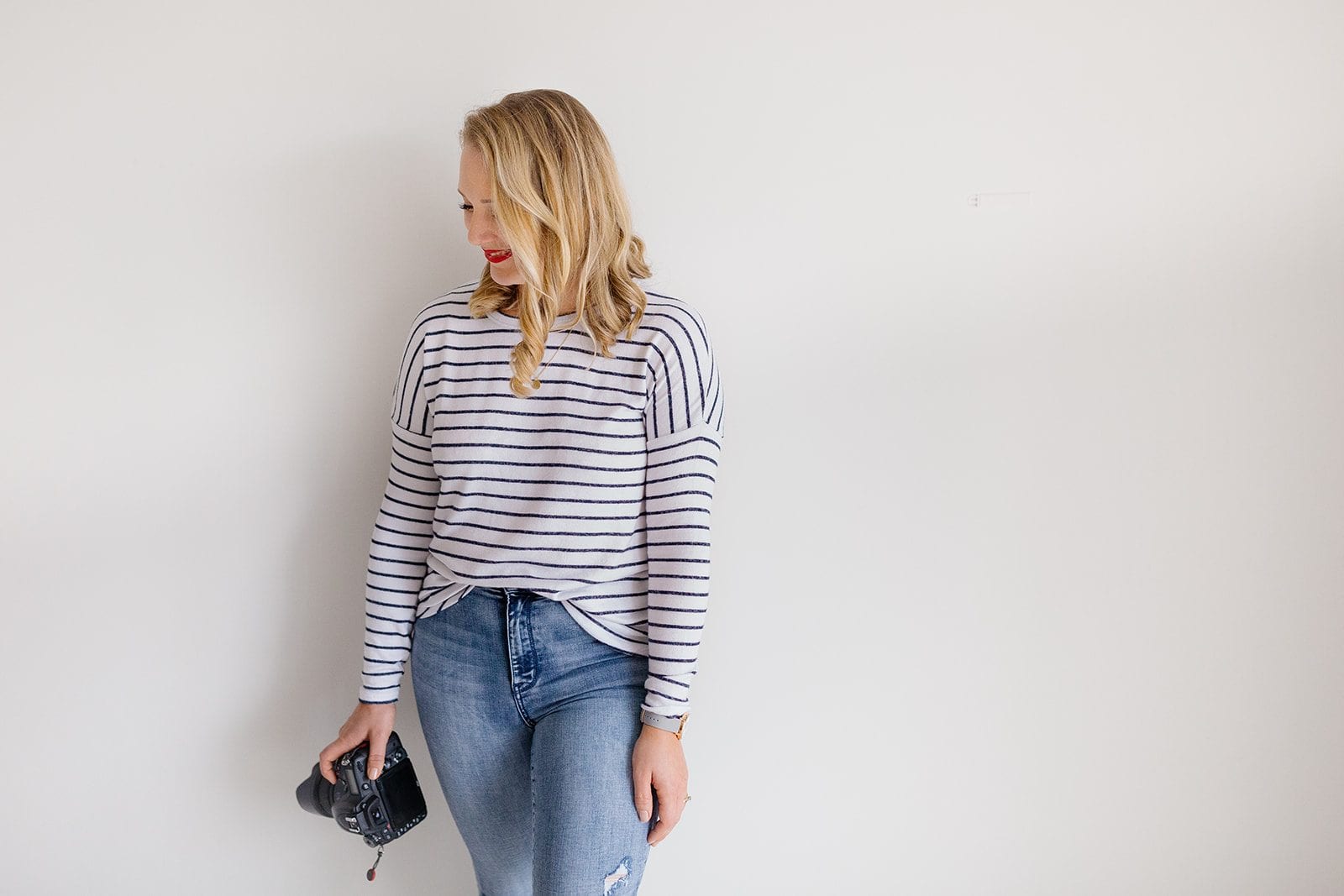 Family photographer Tegan in a striped top holds her camera against a bright studio wall.