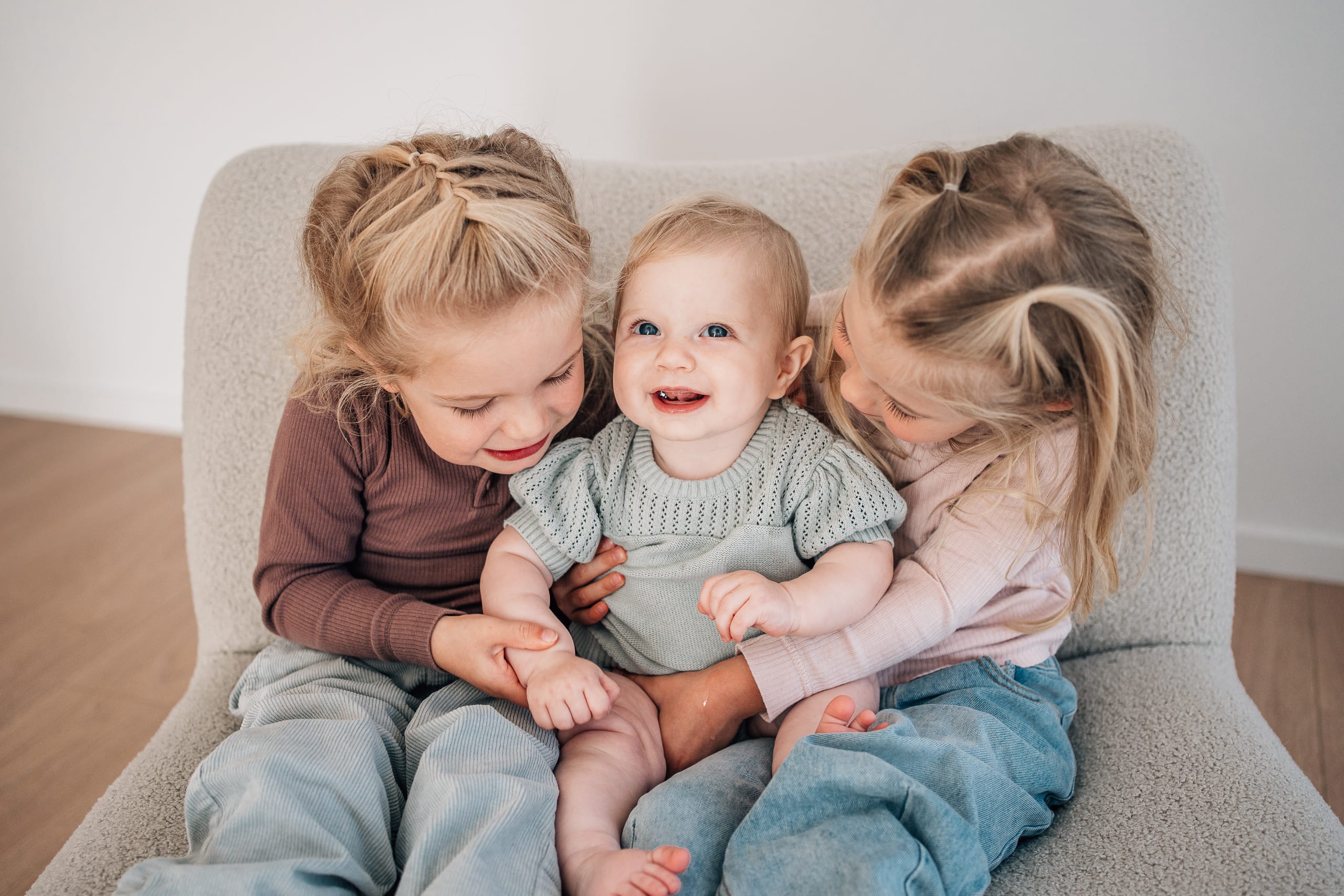 Three young sisters cuddled together laughing during a sibling studio session at The Little White Studio in Lincoln