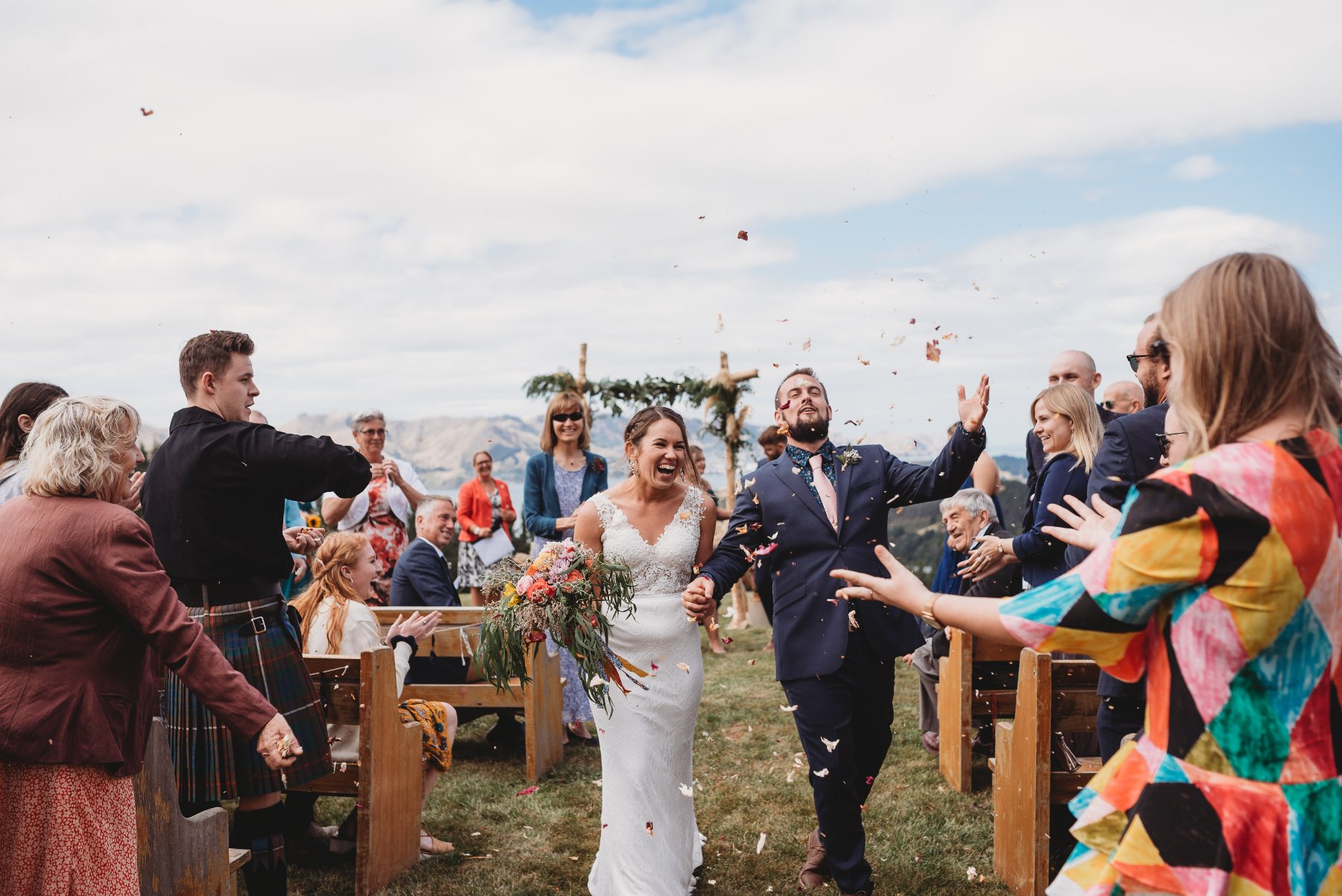 A couple laughing down the aisle as guests throw petals