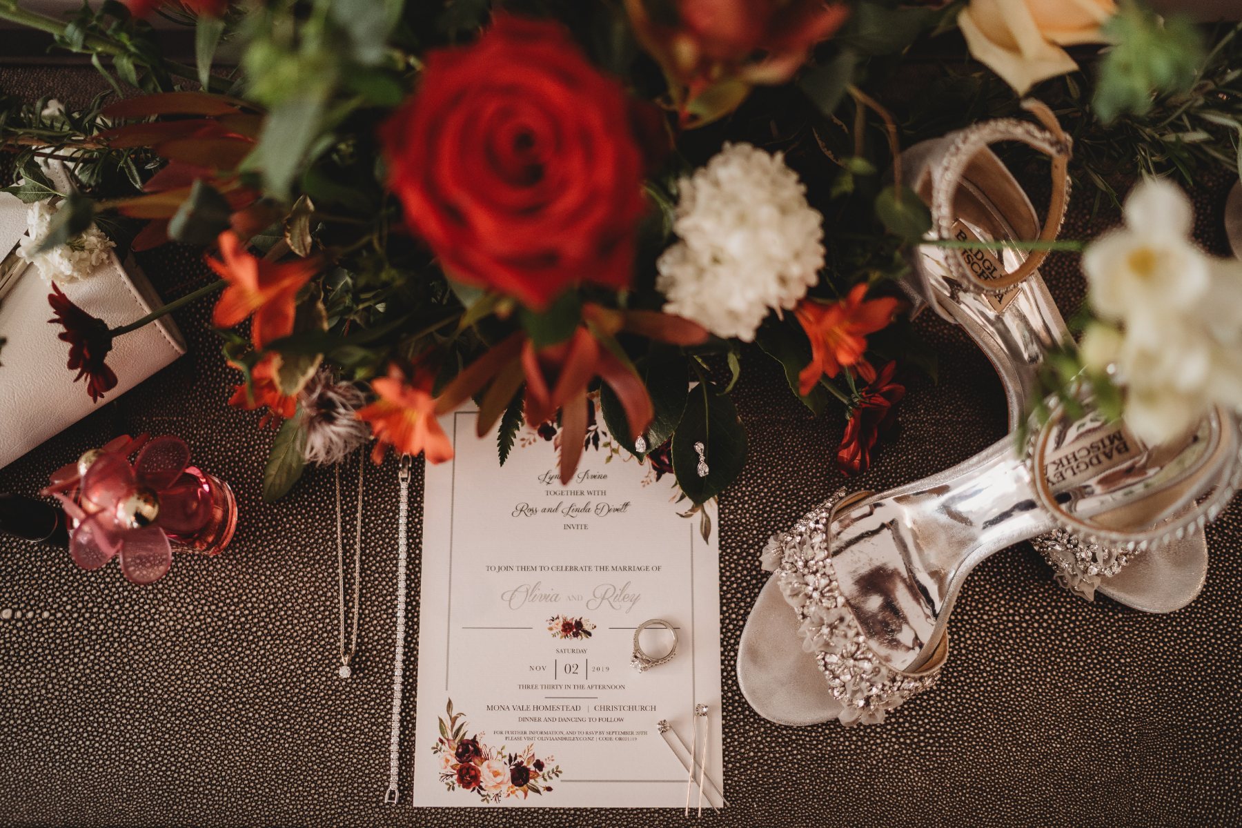 A wedding invitation laid out with rings, earrings, jewellery and sparkly heels among red roses