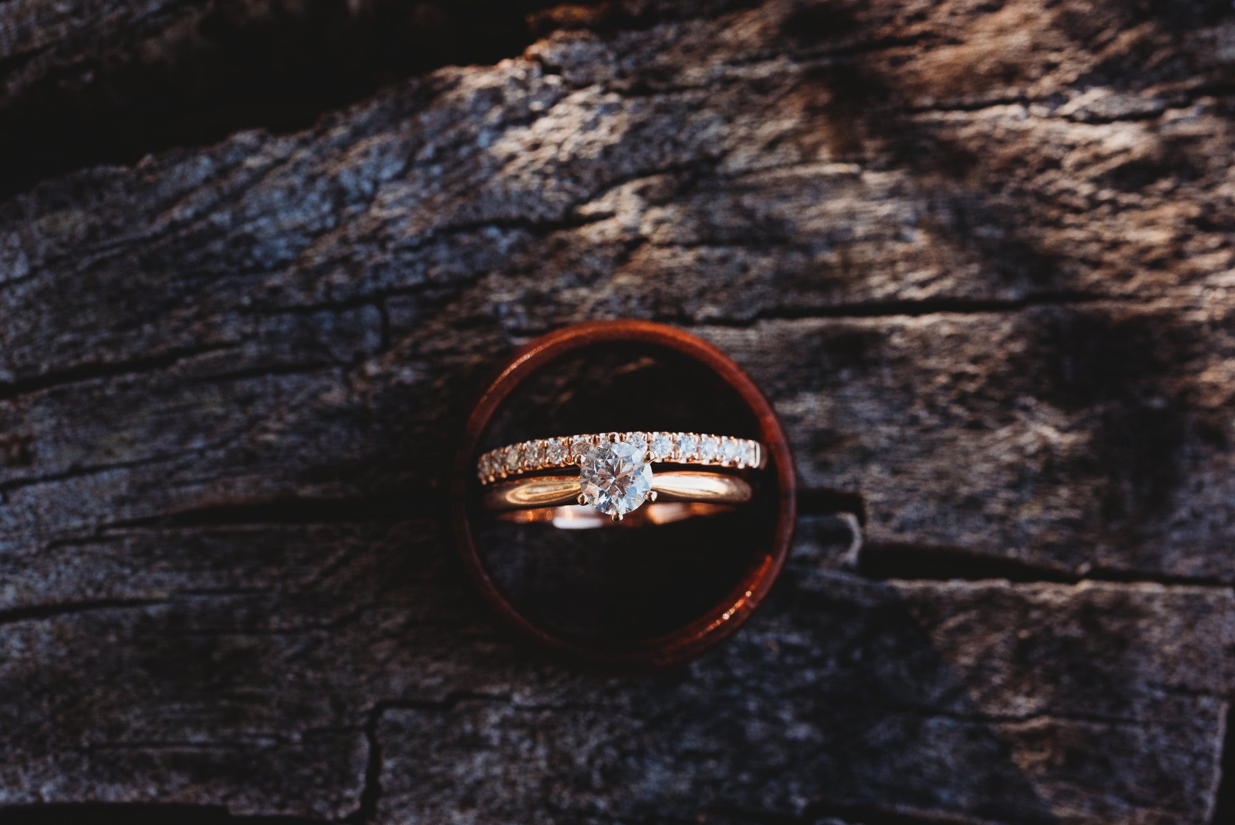 Wedding and engagement rings resting inside a timber band on weathered wood