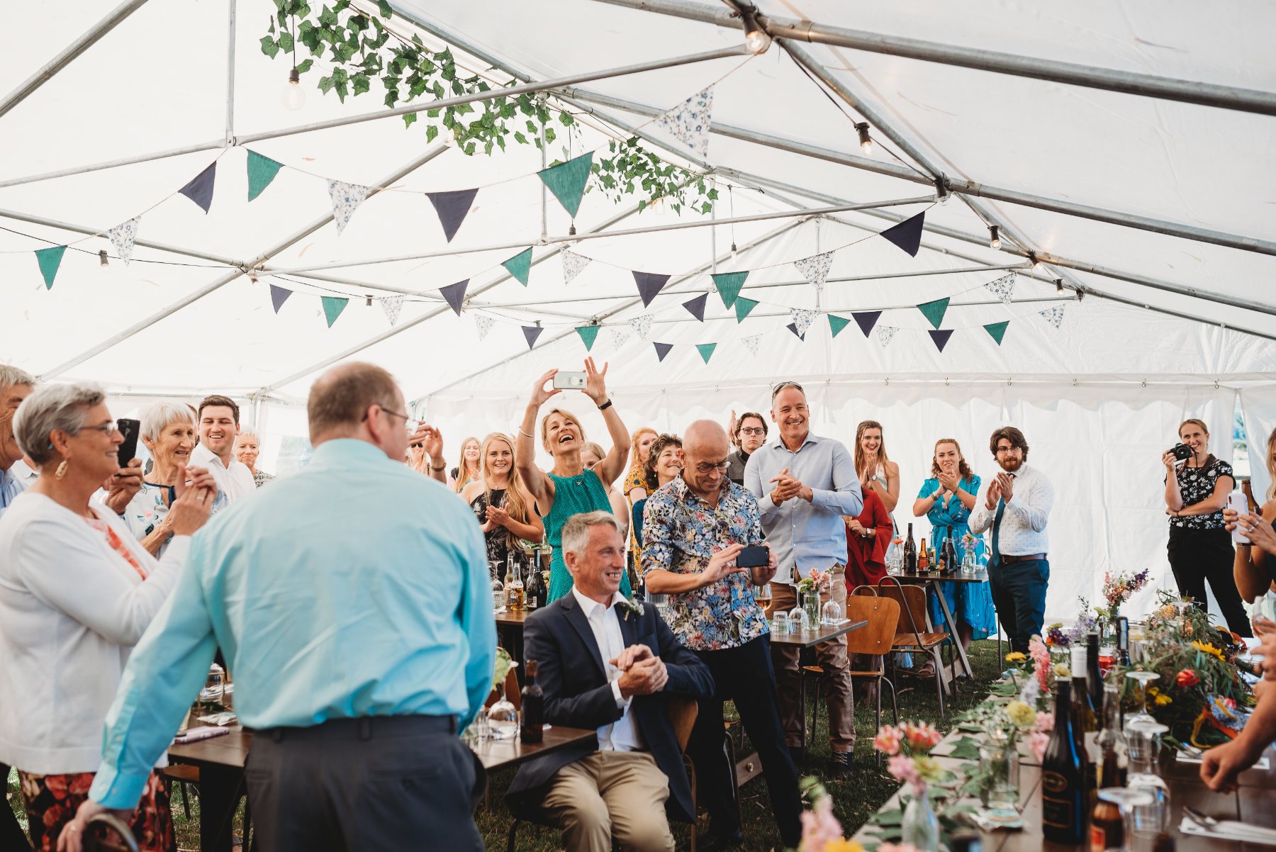Guests on their feet cheering and filming during the speeches in a marquee