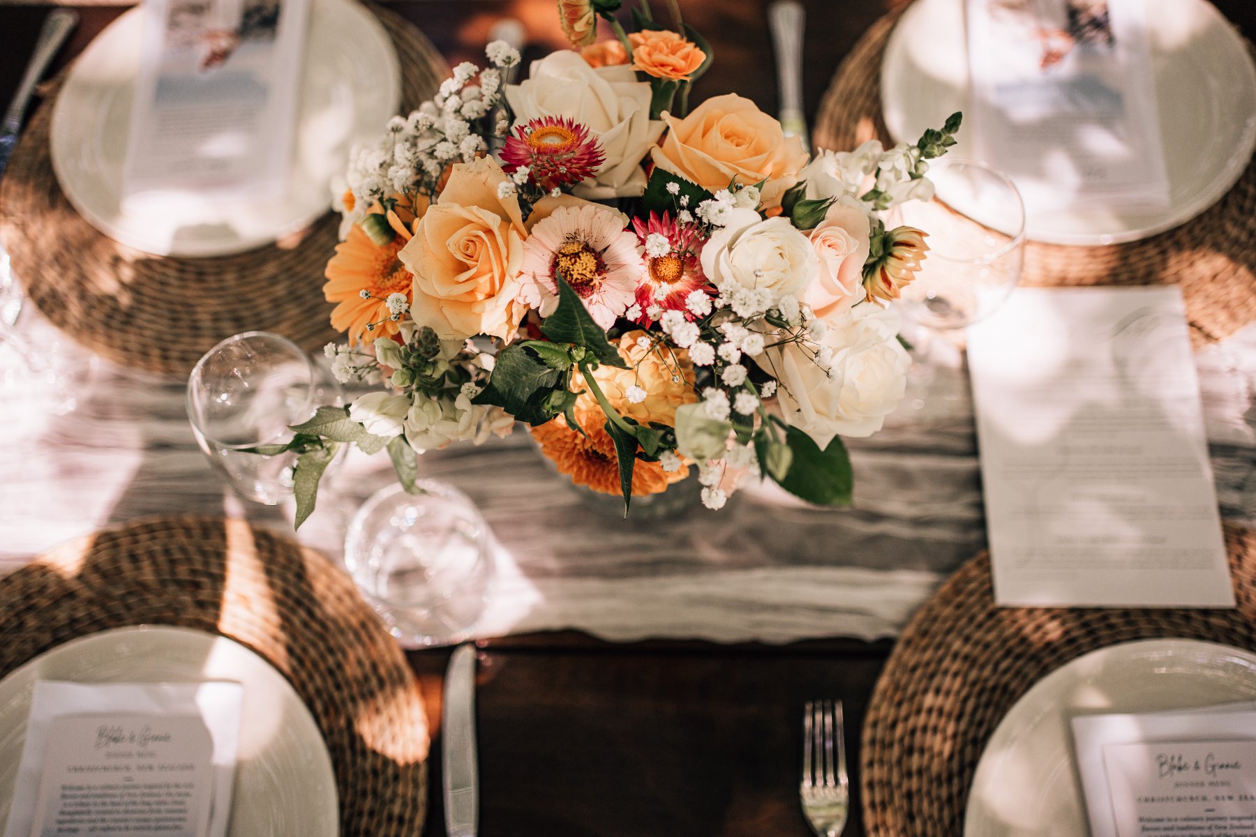 Looking down on a table centrepiece of peach roses and daisies, with woven placemats and menus
