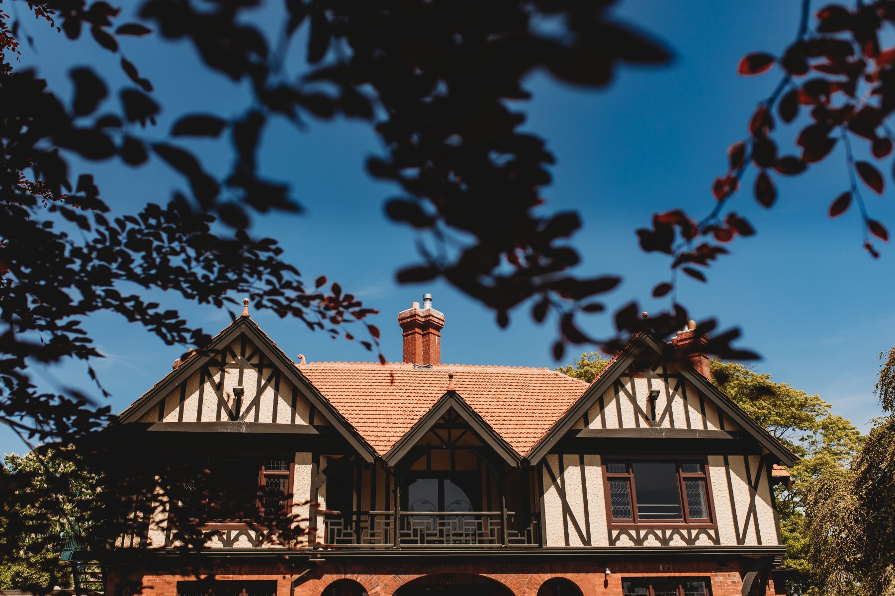A Tudor-style homestead venue framed by leaves against a blue sky