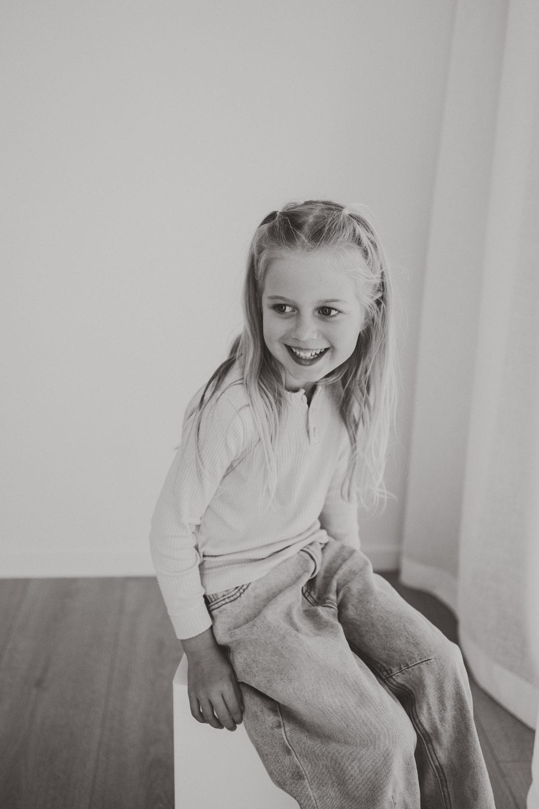 Black and white studio portrait of a blonde young girl smiling and leaning to one side.